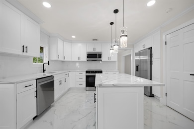 Kitchen featuring light marble finish flooring, appliances with stainless steel finishes, a kitchen island, recessed lighting, and ornamental molding
