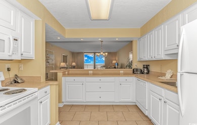 Kitchen with white appliances, a chandelier, hanging light fixtures, white cabinets, and a textured ceiling