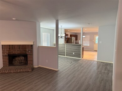 Unfurnished living room with a brick fireplace, dark wood finished floors, and a chandelier
