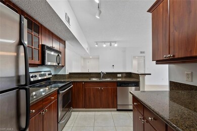 Kitchen with sink, light tile patterned floors, appliances with stainless steel finishes, a textured ceiling, and dark stone counters