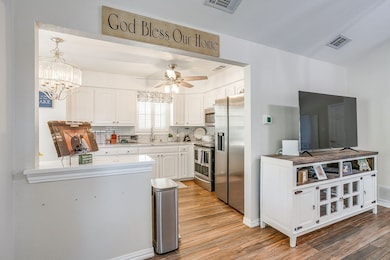 Kitchen with white cabinetry, backsplash, appliances with stainless steel finishes, and light wood-style floors