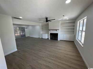 Unfurnished living room featuring a textured ceiling, dark wood-type flooring, built in shelves, a fireplace, and ceiling fan