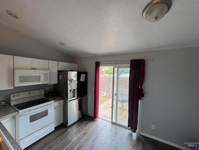 Kitchen with white appliances, white cabinetry, dark wood finished floors, vaulted ceiling, and a textured ceiling