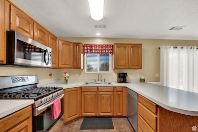 Kitchen featuring appliances with stainless steel finishes, brown cabinetry, a peninsula, light countertops, and a textured ceiling