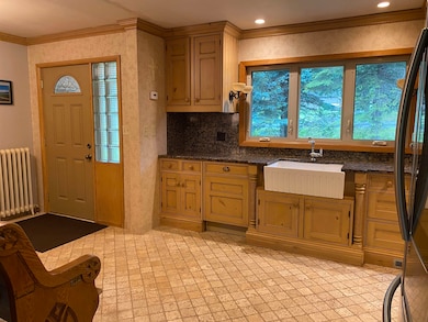 Kitchen featuring radiator, crown molding, freestanding refrigerator, dark stone counters, and tasteful backsplash