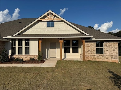 View of front of property with a shingled roof, a porch, brick siding, a front yard, and board and batten siding
