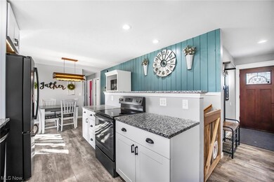 Kitchen with dark wood-type flooring, white cabinetry, stainless steel refrigerator, electric stove, and decorative light fixtures
