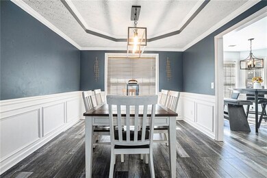 Dining area with a tray ceiling, a decorative wall, dark wood finished floors, a wainscoted wall, and a chandelier