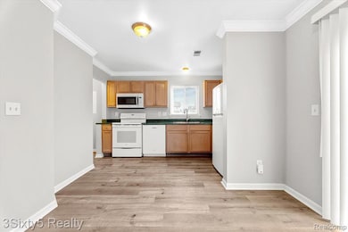 Kitchen featuring white appliances, ornamental molding, dark countertops, light wood-type flooring, and brown cabinets