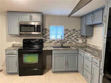 Kitchen with gray cabinets, black electric range, stainless steel microwave, stainless steel counters, and tasteful backsplash