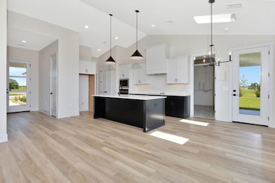 Kitchen with light countertops, a chandelier, built in microwave, white cabinets, and light wood-style flooring
