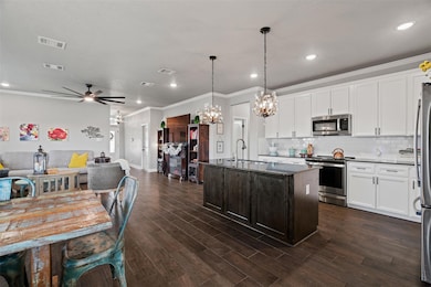 Kitchen featuring open floor plan, crown molding, backsplash, white cabinetry, and appliances with stainless steel finishes