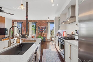 Kitchen featuring stainless steel appliances, wall chimney range hood, brick wall, dark wood-style floors, and white cabinets