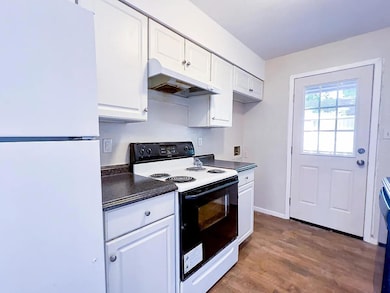 Kitchen with range with electric cooktop, freestanding refrigerator, dark countertops, dark wood-style flooring, and under cabinet range hood