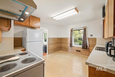 Kitchen with island exhaust hood, white appliances, wainscoting, brown cabinetry, and wood walls