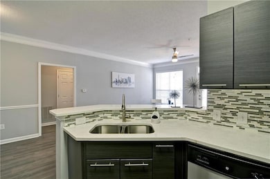 Kitchen featuring ceiling fan, sink, dishwasher, light stone counters, and dark wood-type flooring