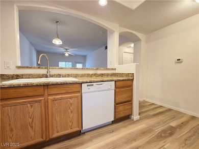 Kitchen featuring white dishwasher, brown cabinetry, light wood-type flooring, and decorative light fixtures