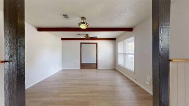 Empty room featuring beamed ceiling, light wood-style floors, a textured ceiling, and a ceiling fan