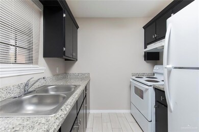 Kitchen featuring light countertops, a sink, dark cabinetry, under cabinet range hood, and white appliances