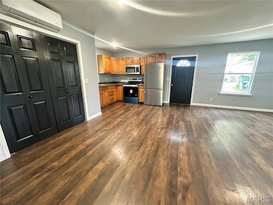 Kitchen featuring a wall mounted AC, stainless steel appliances, dark wood finished floors, brown cabinets, and dark countertops