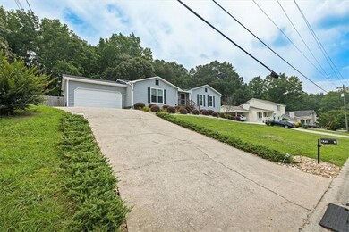 Ranch-style house with driveway, an attached garage, and view of scattered trees