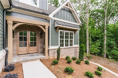 Doorway to property with board and batten siding, brick siding, french doors, and a shingled roof