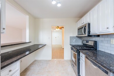 Kitchen with appliances with stainless steel finishes, dark stone counters, light tile patterned floors, tasteful backsplash, and white cabinetry