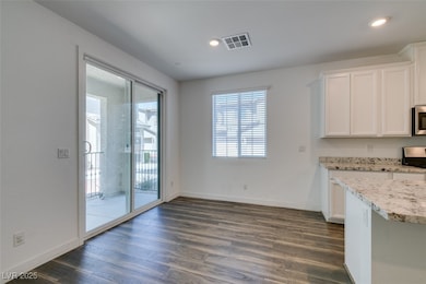 Kitchen featuring white cabinets, visible vents, baseboards, stainless steel microwave, and dark wood-type flooring