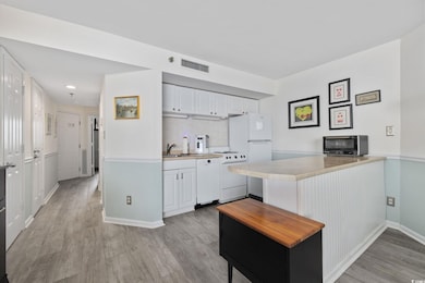 Kitchen featuring white appliances, white cabinetry, light countertops, light wood-style flooring, and tasteful backsplash