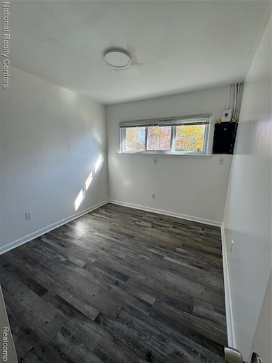 Empty room featuring dark wood-style floors and baseboards