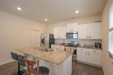 Kitchen with appliances with stainless steel finishes, dark wood-style floors, white cabinetry, an island with sink, and recessed lighting