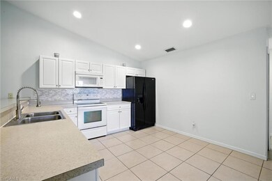 Kitchen with white appliances, tasteful backsplash, vaulted ceiling, white cabinets, and light countertops