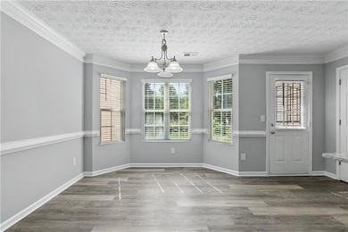 Unfurnished dining area with light wood finished floors, crown molding, a textured ceiling, and a chandelier