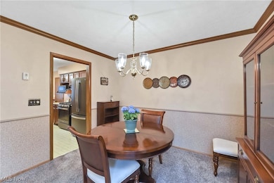 Carpeted dining area featuring ornamental molding and a notable chandelier
