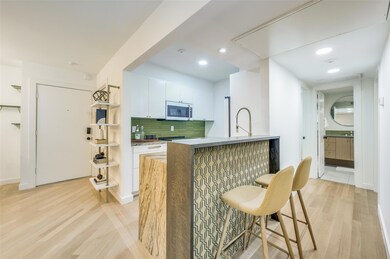 Kitchen featuring kitchen peninsula, light wood-type flooring, backsplash, a kitchen bar, and white cabinetry