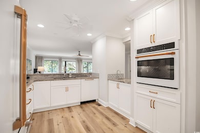 Kitchen with white appliances, white cabinets, ornamental molding, light stone counters, and light wood-style flooring