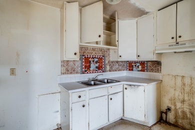Kitchen featuring tasteful backsplash, light countertops, open shelves, white cabinets, and under cabinet range hood
