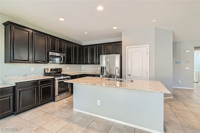 Kitchen with stainless steel appliances, light tile patterned floors, a center island with sink, light stone countertops, and recessed lighting