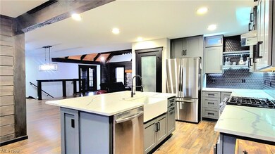 Kitchen with light hardwood / wood-style floors, light stone countertops, hanging light fixtures, a center island with sink, and beamed ceiling