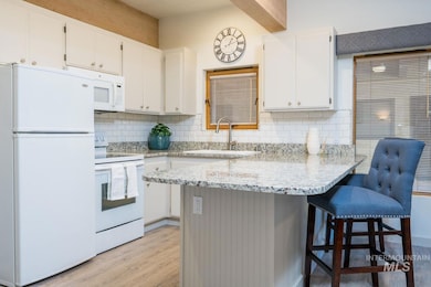 Kitchen featuring white appliances, light wood-style flooring, white cabinets, a peninsula, and decorative backsplash