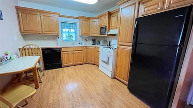 Kitchen with black appliances, tile counters, light wood-type flooring, a sink, and under cabinet range hood