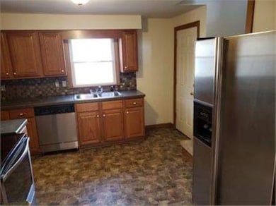 Kitchen featuring stainless steel appliances, brown cabinets, backsplash, and dark countertops