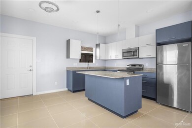 Kitchen with appliances with stainless steel finishes, a kitchen island, light countertops, light tile patterned floors, and decorative light fixtures