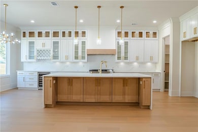 Kitchen with glass insert cabinets, pendant lighting, white cabinetry, a large island with sink, and tasteful backsplash