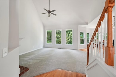 Unfurnished living room with plenty of natural light, ceiling fan, high vaulted ceiling, stairway, and carpet floors