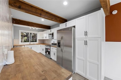 Kitchen with beamed ceiling, wooden counters, white cabinetry, stainless steel appliances, and light wood-style flooring