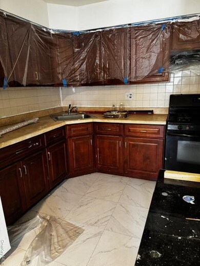 Kitchen featuring light marble finish flooring, stove, decorative backsplash, light countertops, and reddish brown cabinets
