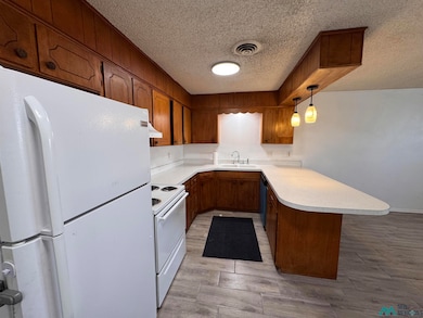 Kitchen with white appliances, light countertops, a peninsula, a textured ceiling, and wood tiled floors