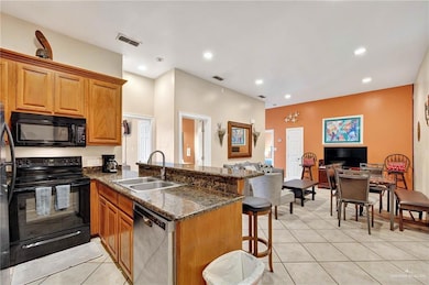 Kitchen with black appliances, a sink, a peninsula, a kitchen bar, and light tile patterned floors