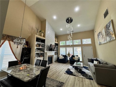 Dining space featuring high vaulted ceiling, a glass covered fireplace, light wood finished floors, a chandelier, and recessed lighting